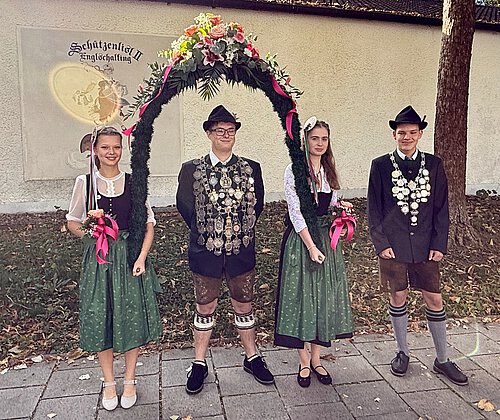Das Bild zeigt unseren Schützenkönig Tom Painter unter dem Bogen gehalten von seinen Liesln Sophie Meier und Sarah Schmier. Zusätzlich zeigt es den Jugendkönig. Beide Könige haben Ihre Schützenkette bestehend aus vielen Talern umgehängt