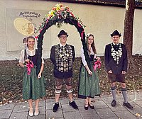 Das Bild zeigt unseren Schützenkönig Tom Painter unter dem Bogen gehalten von seinen Liesln Sophie Meier und Sarah Schmier. Zusätzlich zeigt es den Jugendkönig. Beide Könige haben Ihre Schützenkette bestehend aus vielen Talern umgehängt