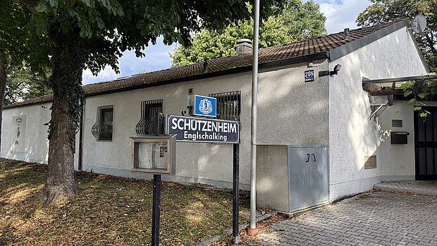 Das Bild zeigt das Vereinsheim von der Seite. Man sieht rechts den Eingang, in der Mitte das Vereinschilld und hinten links das Vereinslogo an der Wand